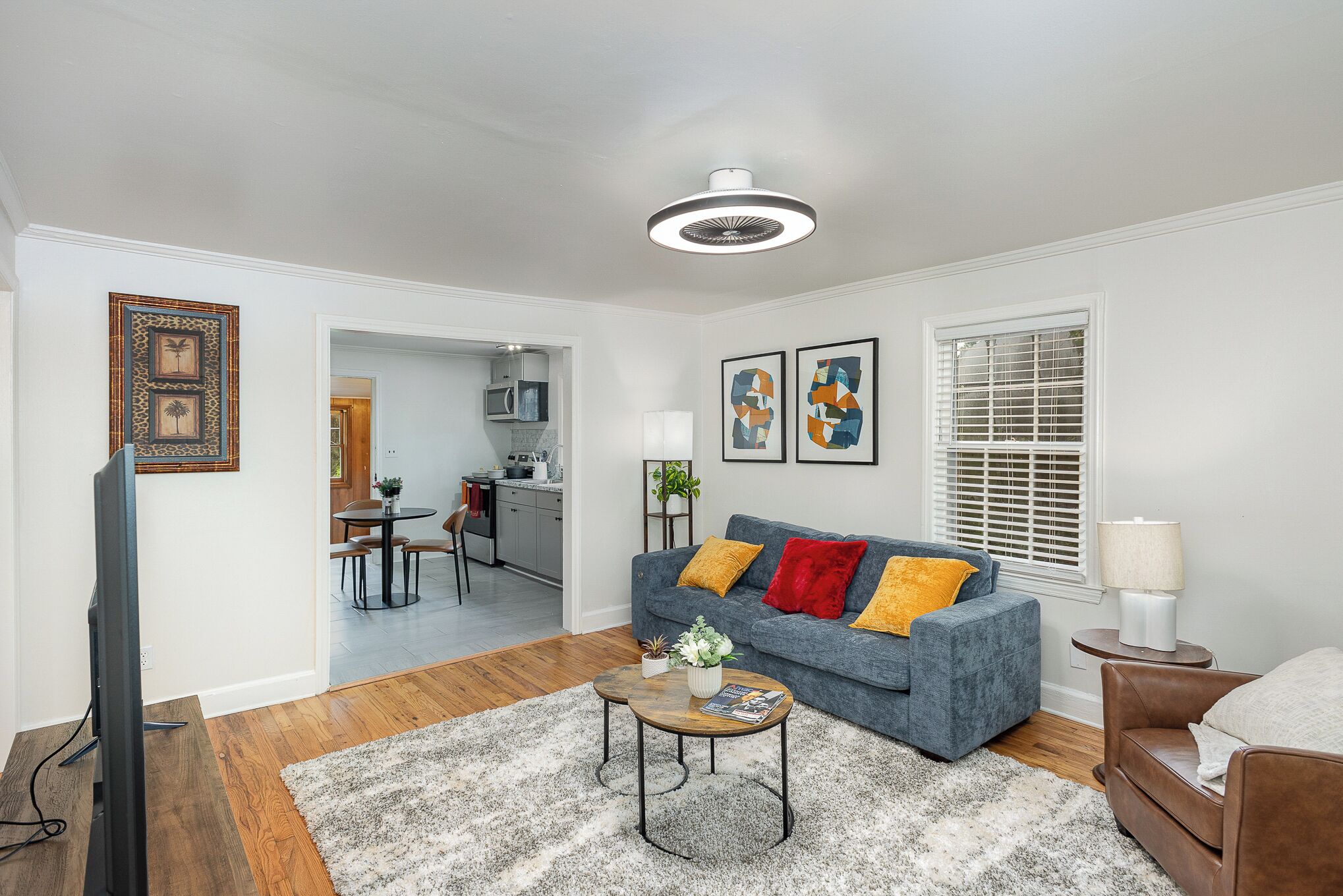 A modern living room with a grey sofa, a coffee table, and a TV. There is a kitchen in the background.