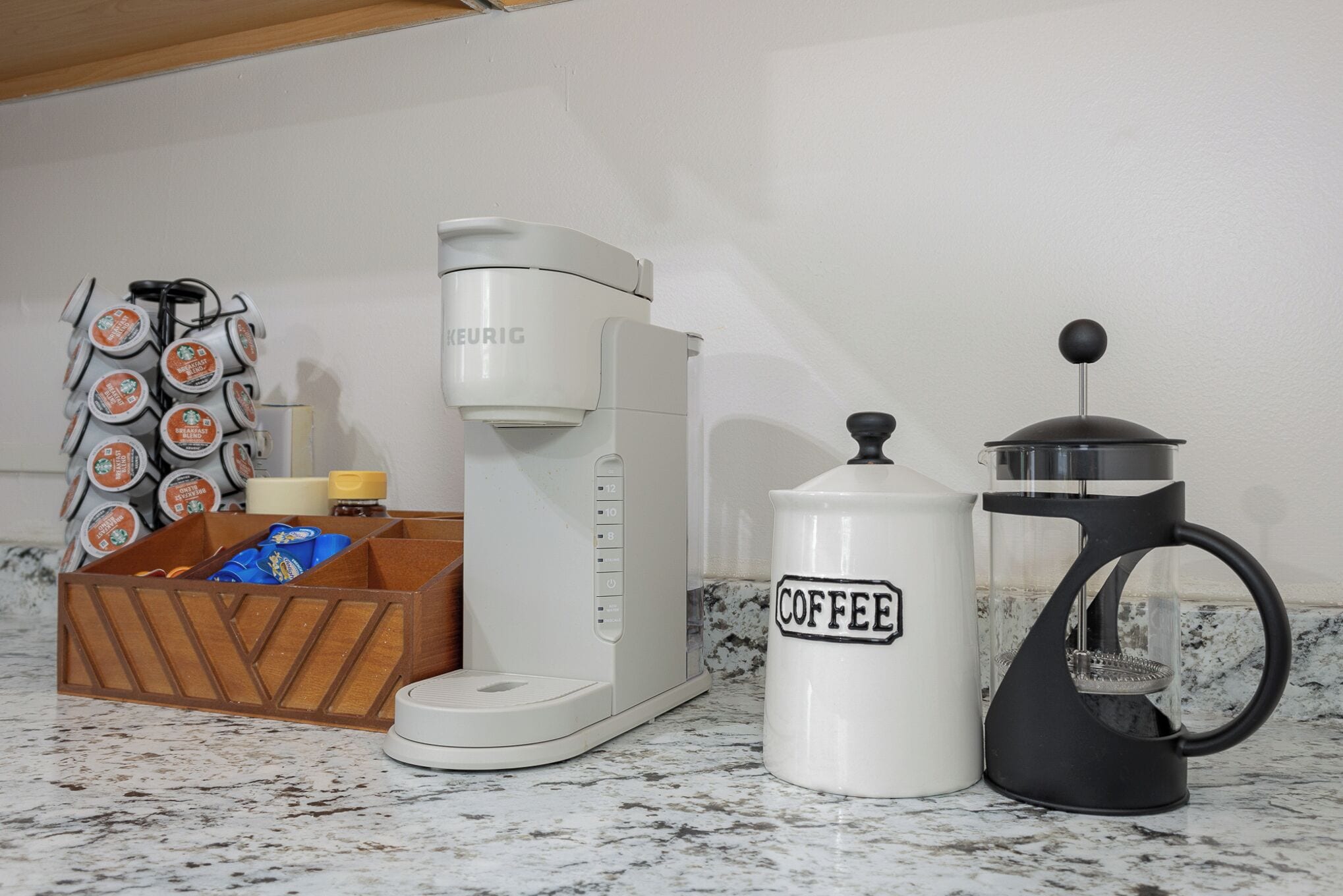 A coffee maker, a coffee grinder, and a box of coffee pods on a kitchen counter.