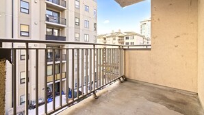 A balcony with a metal railing, a concrete floor, and a view of adjacent buildings. - Bright 2 Bedroom Suite at Victoria & Stampede Park (Calgary)