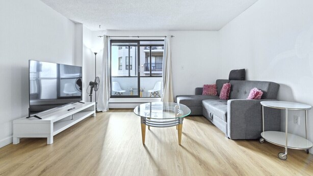 A modern living room with a flat-screen TV, a glass coffee table, a grey sofa, and a small side table. - Bright 2 Bedroom Suite at Victoria & Stampede Park (Calgary)
