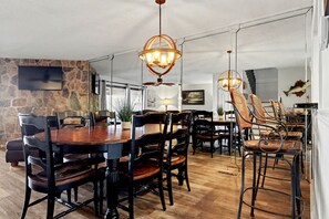 A dining area with a large wooden table, black chairs, wicker chairs, and a stone accent wall.