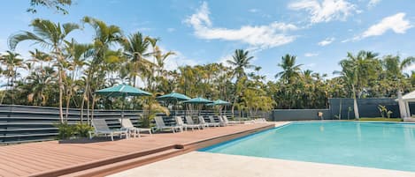 A swimming pool with lounge chairs and umbrellas, surrounded by palm trees.
