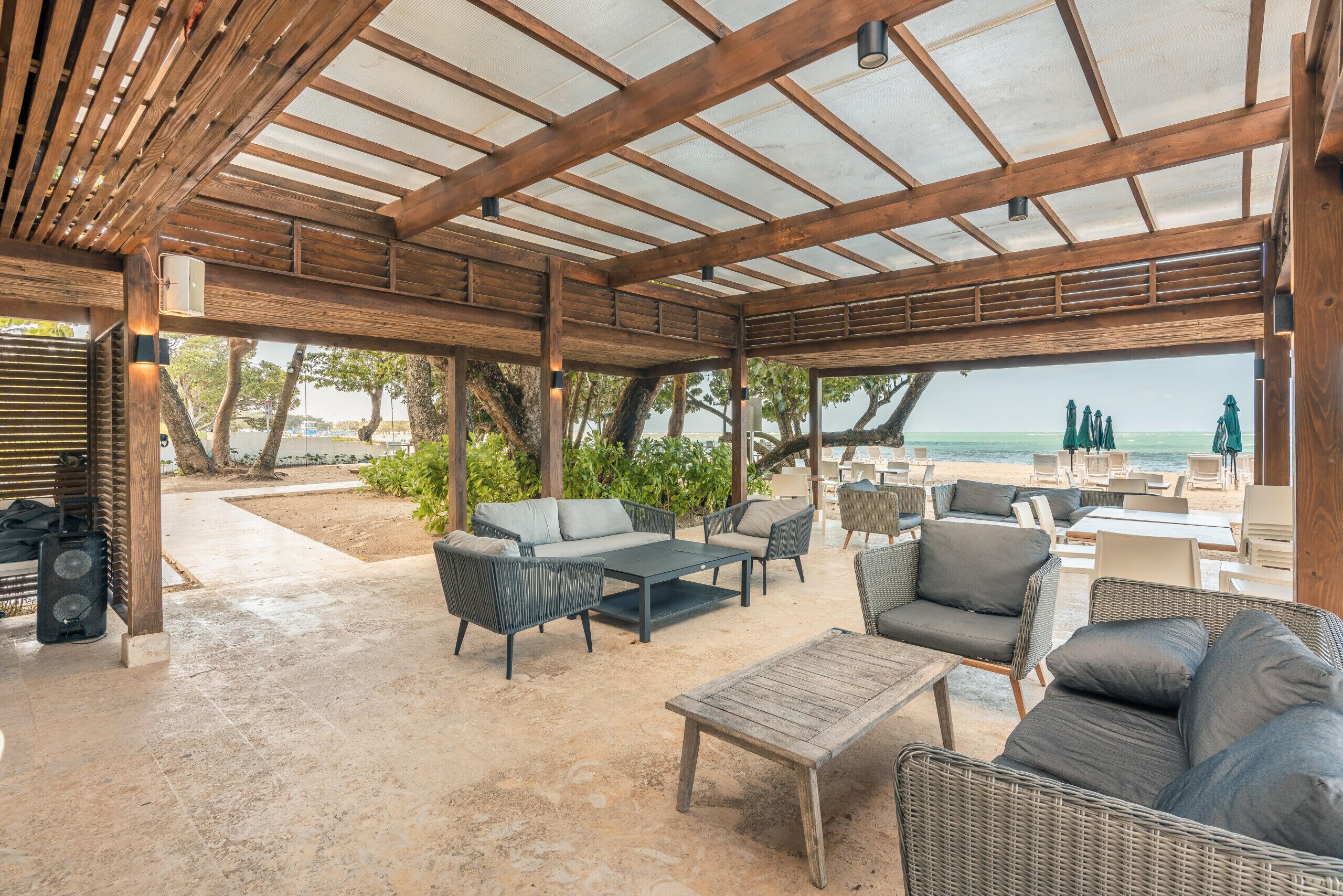 Un espace extérieur aménagé avec des poutres en bois, des meubles en osier et une vue sur la plage.