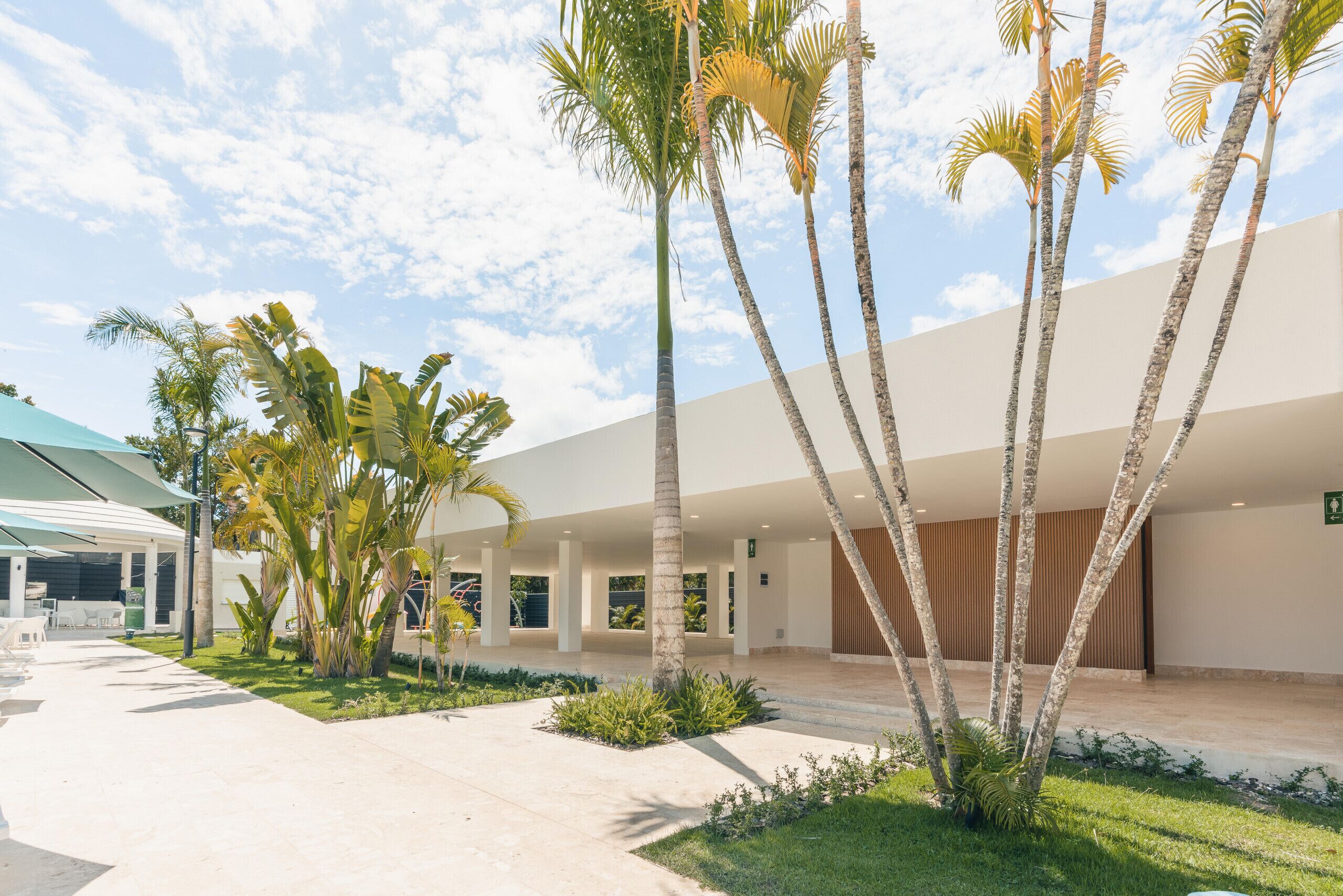 A hotel lobby with palm trees, a covered seating area, and a modern building facade.