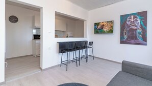 A modern living room with a grey sofa, a dining area with three black chairs, a kitchen in the background, and a large abstract painting on the wall. - Aurelius - Superior sea view apartment (Konavle)