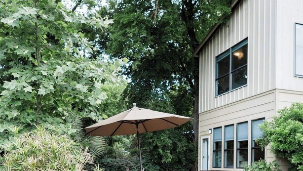 Un patio con mobiliario exterior, un paraguas grande y una jardinera con etiqueta.