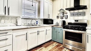 Una cocina con armarios blancos, estufa de acero inoxidable, microondas y piso de madera.