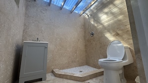 Une petite salle de bain comprenant une douche, des toilettes et un petit meuble de rangement.