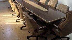Een vergaderruimte met een lange tafel en zes stoelen, een scherm voor een beamer en een deur op de achtergrond.