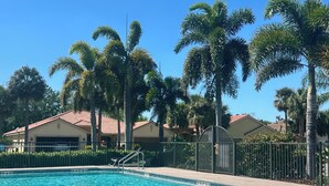 A clear swimming pool with a 5 ft depth marking, surrounded by palm trees and houses with red roofs.