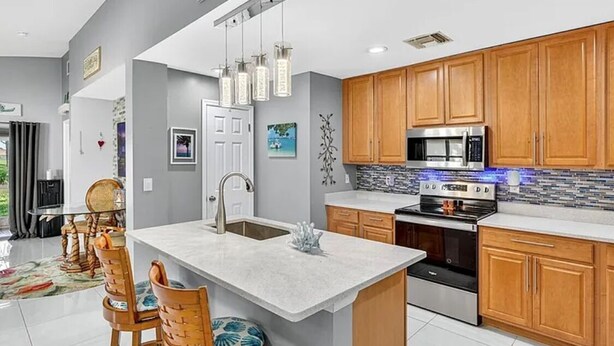 A modern kitchen with wooden cabinets, a central island, stainless steel appliances, and pendant lighting.