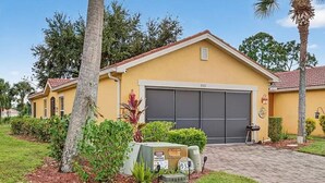 A yellow house with a garage, surrounded by well-maintained lawns and palm trees.