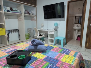 Ein Schlafzimmer mit Bett, Schreibtisch, Stuhl, Fernseher und eigenem Badezimmer.