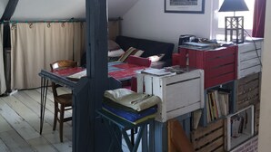 Ein gemütliches Dachzimmer mit schrägverlaufender Decke, einem gerahmten Stadtbild, einer roten Lampe und einer Holzleiter.