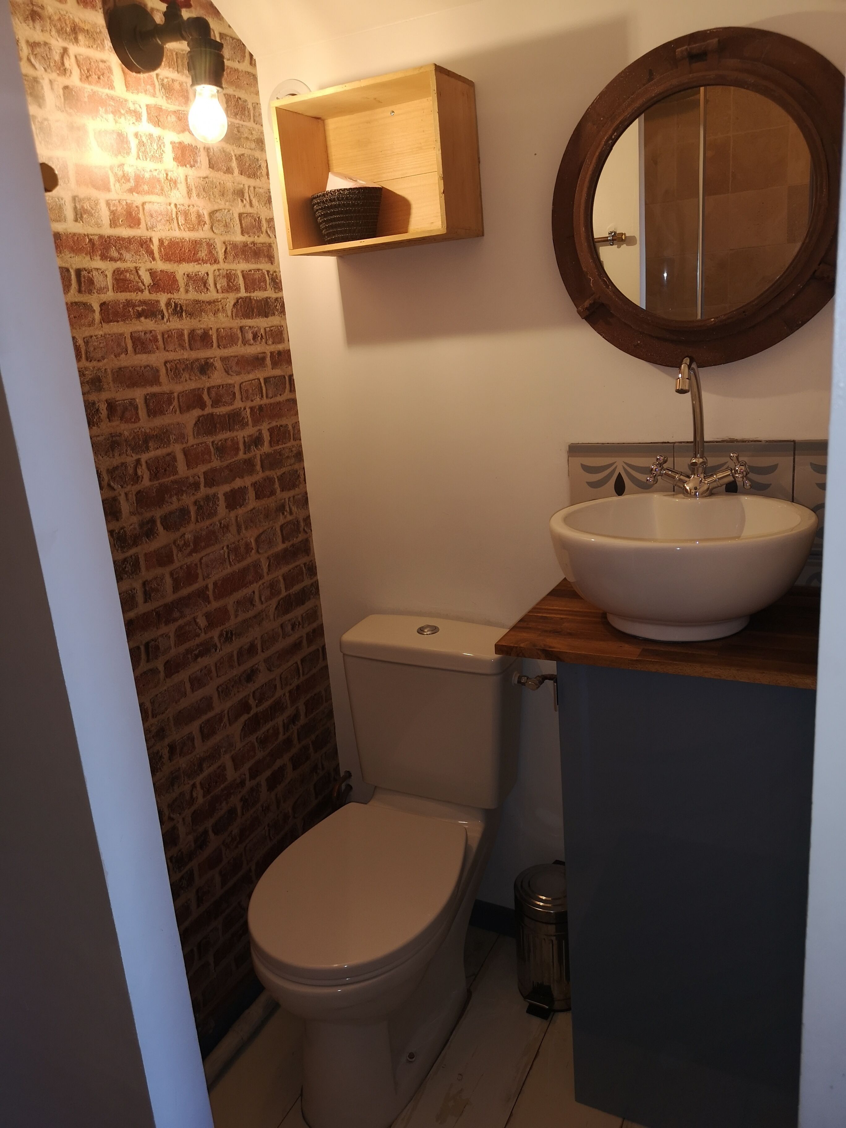 A bathroom with a toilet, a sink with a mirror, and a light fixture on the wall.