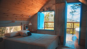 Un dormitorio de cabaña de madera con cama, ventana y vistas a los árboles.