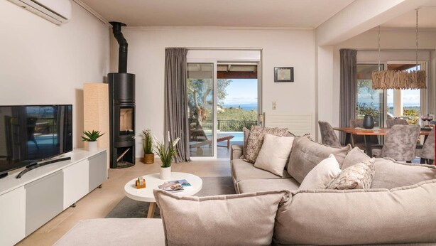 Una sala de estar moderna con sofá, televisor y chimenea. Hay un balcón con vistas al mar.