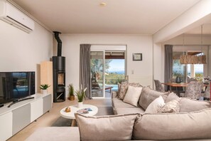 A modern living room with a sofa, TV, and fireplace. There is a balcony with a view of the sea.