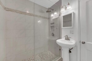 A modern bathroom with a glass-enclosed shower, a white sink, and a mirror above it. - Victoria Park Oasis Walk to las Olas  Beach (Fort Lauderdale)