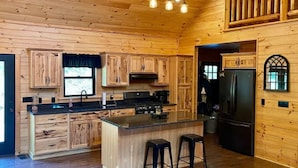Cucina in stile baita di legno con pareti in legno, isola centrale con sgabelli e frigorifero.