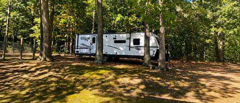 A recreational vehicle (RV) parked in a wooded area with a fenced enclosure.