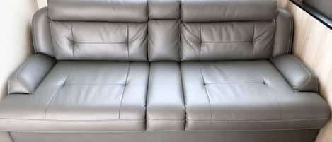 A grey leather sofa with a high backrest and armrests, positioned against a wall with a window.