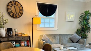 A living room with a wooden dining table, chairs, a sofa, a coffee table, a clock, a lamp, and a world map on the wall.