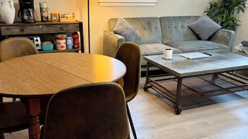 A living room with a wooden dining table, chairs, a sofa, a coffee table, a clock, a lamp, and a world map on the wall.