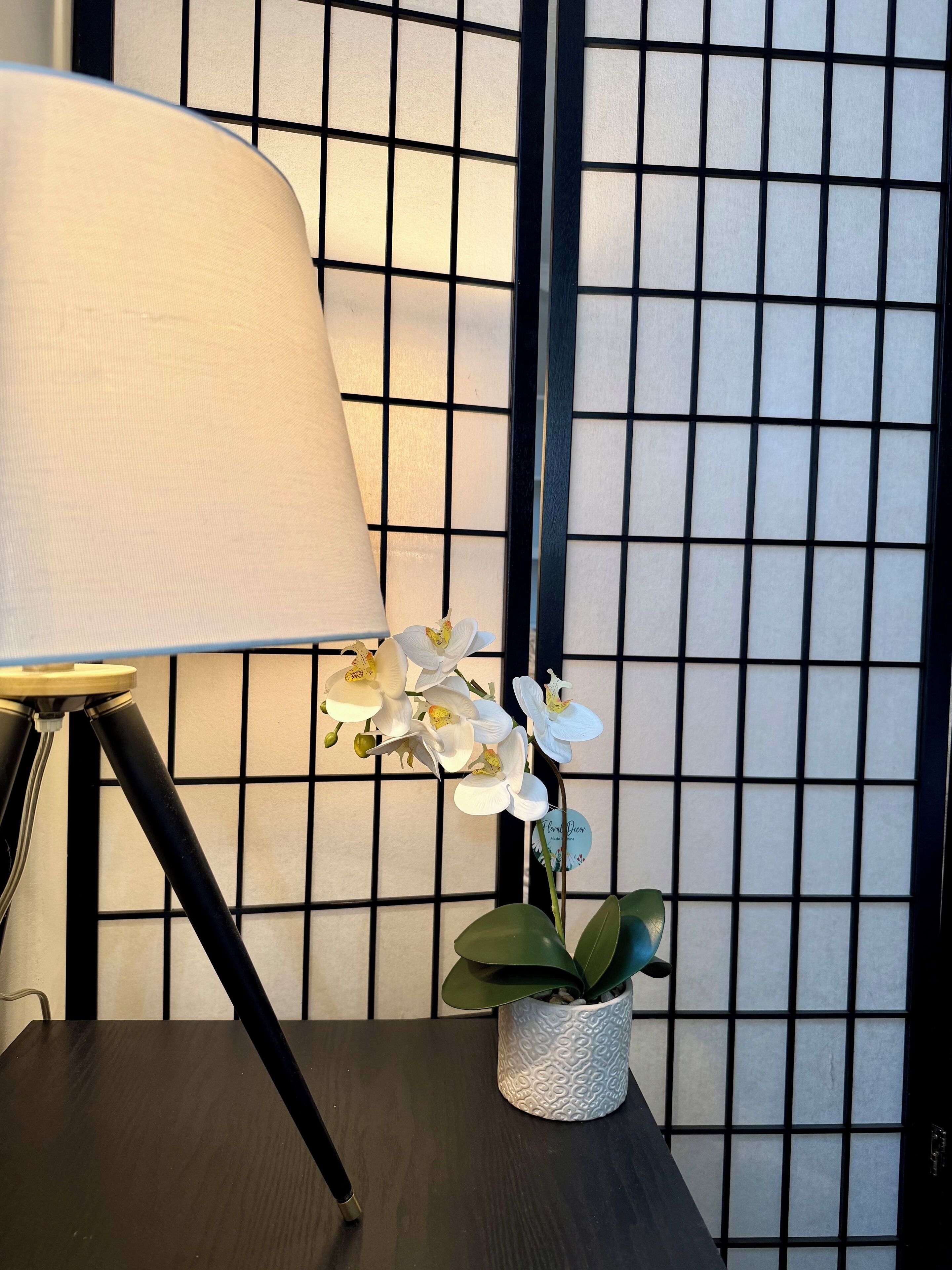 Een lamp op een tafel met een bloeiende orchidee en een decoratieve wand met een rasterpatroon.