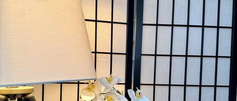 Een lamp op een tafel met een bloeiende orchidee en een decoratieve wand met een rasterpatroon.