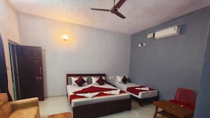 Un dormitorio con dos camas individuales, un banco de madera, una silla roja, un ventilador de techo y un equipo de aire acondicionado.