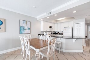 A modern kitchen with white cabinetry, a central island, and a dining area with a wooden table and white chairs. - San Carlos 1905 |Beach Front (Gulf Shores)