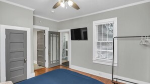 Une chambre à coucher avec un lit, un ventilateur de plafond, une télévision et une fenêtre avec des stores.