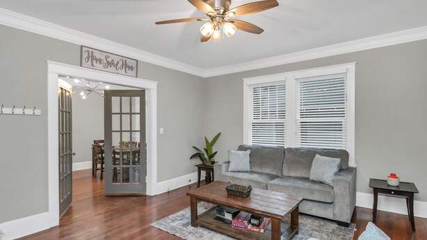 Un salon avec un canapé gris, une table basse, un ventilateur de plafond et un coin repas comprenant une table et des chaises.