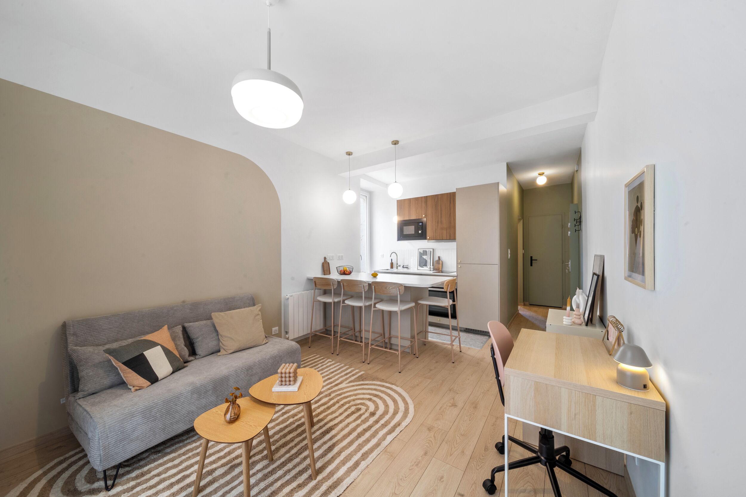 A modern living room with a grey sofa, a small round table, and a kitchen area in the background.