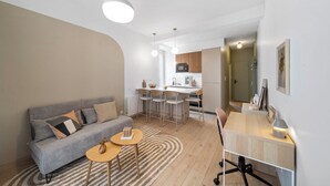 A modern living room with a grey sofa, a small round table, and a kitchen area in the background. - Mabulle: Charming, comfortable apartment in the heart of Dijon - 4 Voyageurs (Dijon)