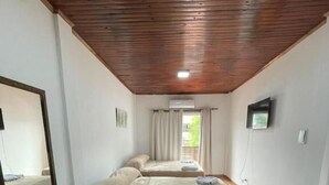 Una habitación con dos camas, piso de madera, ventilador de techo, televisor y ventana con cortinas.