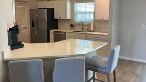 Una cocina moderna con una isla central, dos taburetes de bar y un refrigerador.