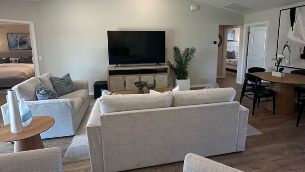Un salón amplio con un televisor de pantalla plana grande, un ventilador de techo y una zona de comedor con una mesa redonda y sillas.