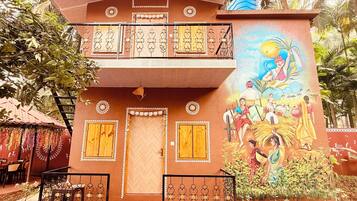 Um edifício de dois andares com varanda, um mural representando cenas rurais e uma porta com padrão decorativo.