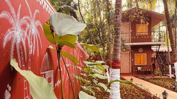 A building with a red exterior and white decorative patterns, surrounded by lush greenery and palm trees.
