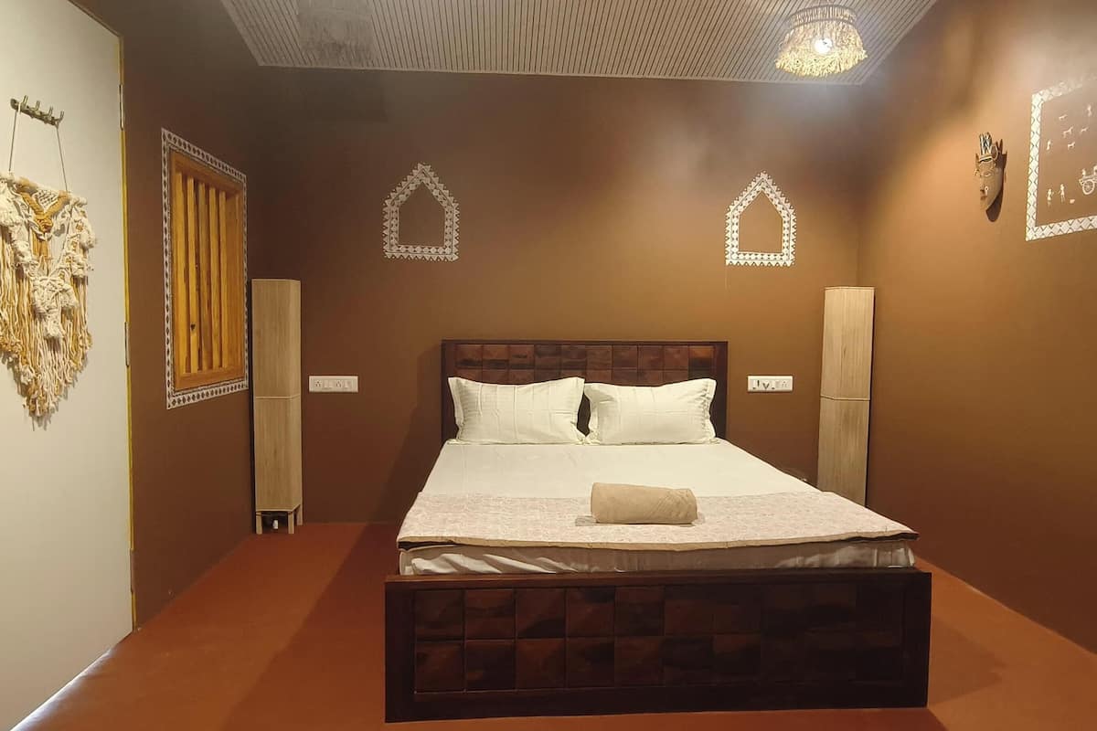 Una cama bien tendida con sábanas blancas y un cojín decorativo, cabecera de madera y un espejo montado en la pared.