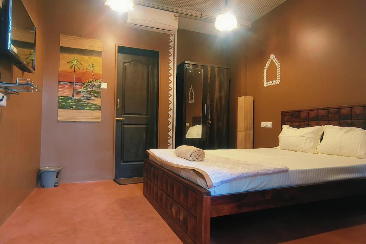 Un dormitorio con cama de madera, un armario oscuro, un cuadro y un pequeño cubo de basura.