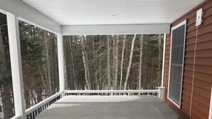 A hot tub on a wooden deck with a railing, surrounded by trees. - Beautiful 6-bedroom house in Rangeley perfect for friends and family getaways. (Rangeley)