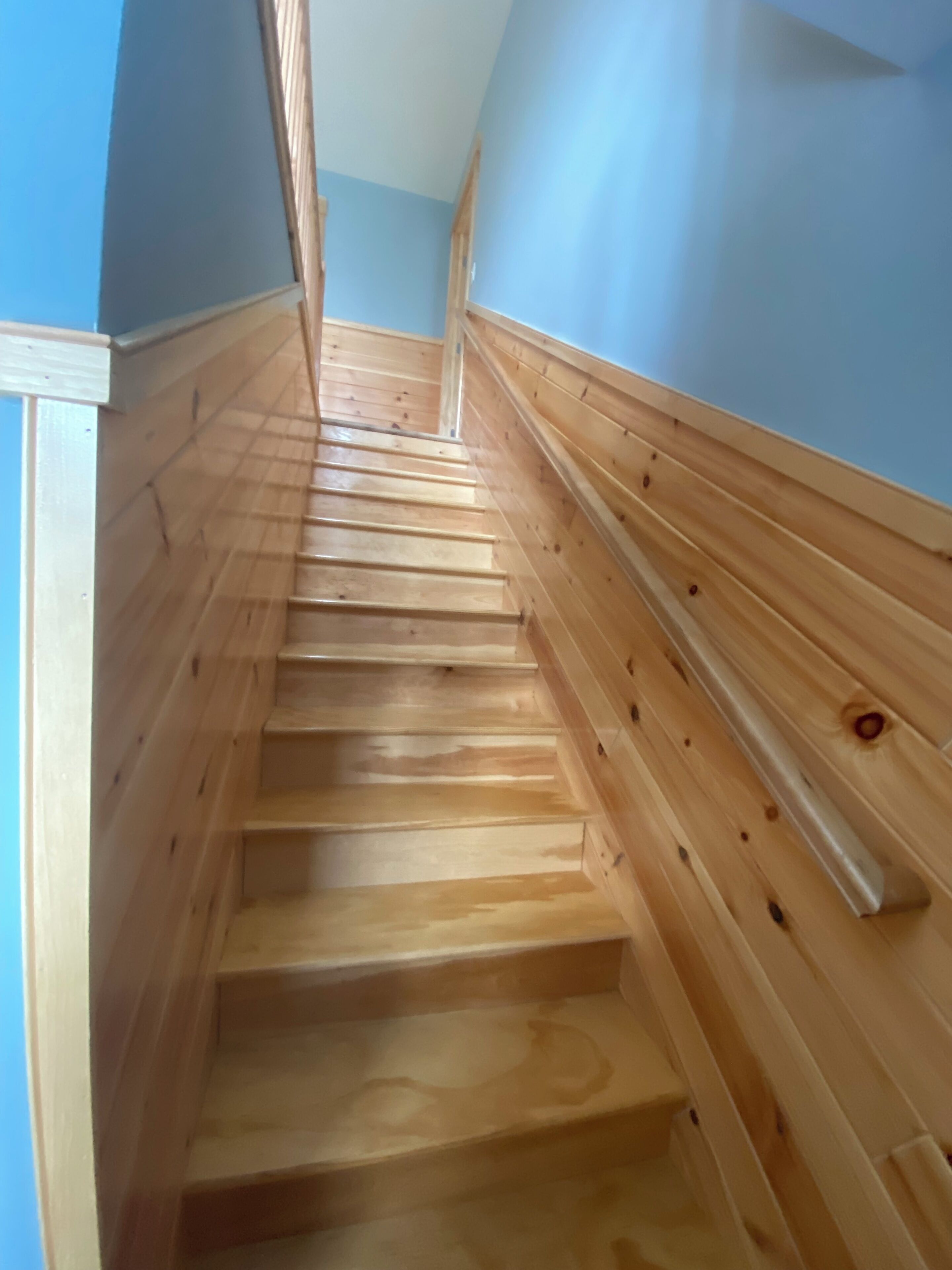 Een houten trap met een leuning, die omhoog leidt.