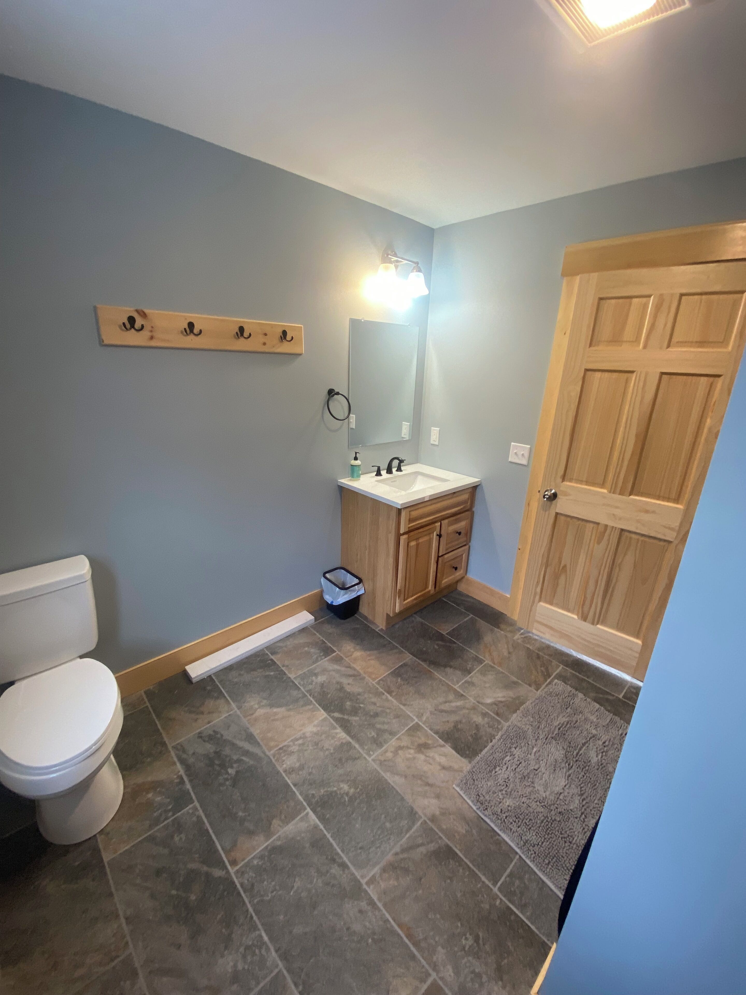 Un baño con inodoro, lavamanos, espejo y puerta de madera.