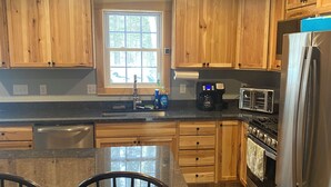 A modern kitchen with wooden cabinets, a stainless steel refrigerator, a built-in oven, and a large window providing natural light. - Beautiful 6-bedroom house in Rangeley perfect for friends and family getaways. (Rangeley)