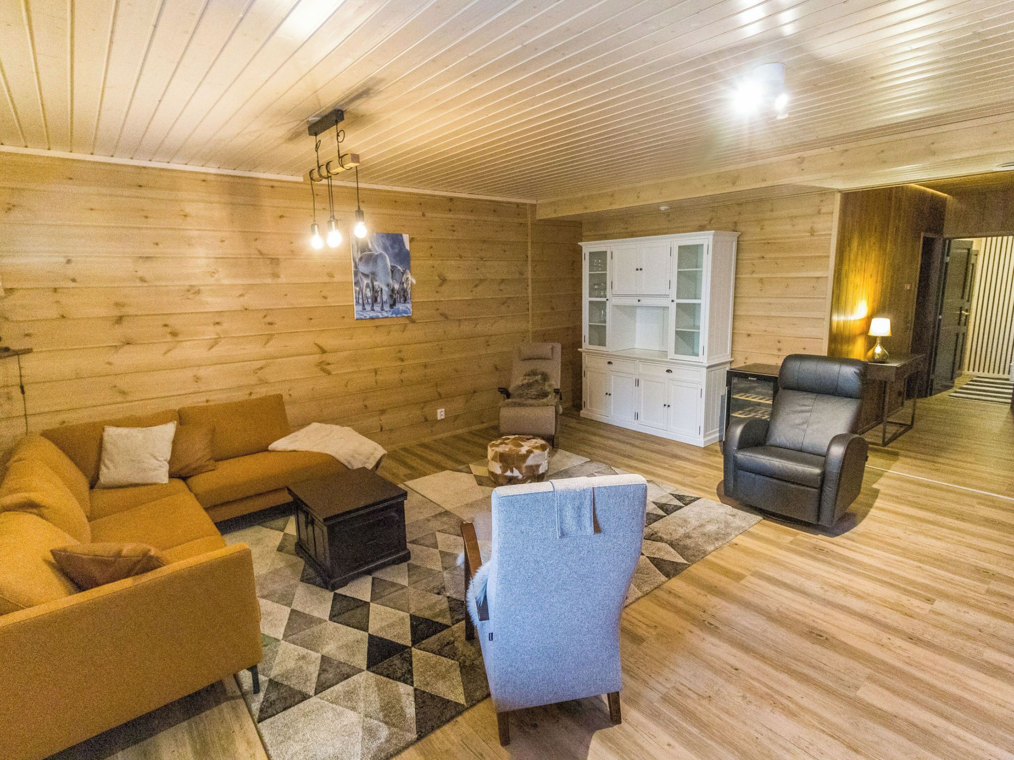A cozy room with wooden walls and floors, a sofa, a chair, a cabinet, and a rug.