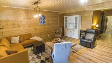 A cozy room with wooden walls and floors, a sofa, a chair, a cabinet, and a rug.