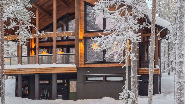 Une maison de style rustique moderne, à plusieurs niveaux, dotée de grandes fenêtres et entourée d’un paysage enneigé.